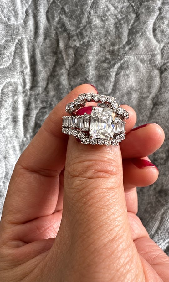 Side angle of the white sapphire three-piece wedding set held between fingers